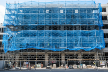 Load image into Gallery viewer, Building under construction with blue scaffolding and safety netting.